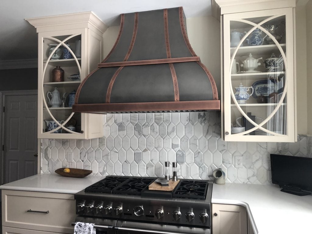 Copper-accented hood flanked by glass-fronted cabinets